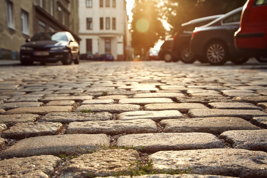 Pflastersteinstraße mit parkenden Autos in abendlicher Sonnenbeleuchtung.