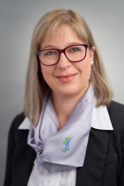 Frau mit blondem Haar, Brille und cds-Halstuch im Business-Outfit.