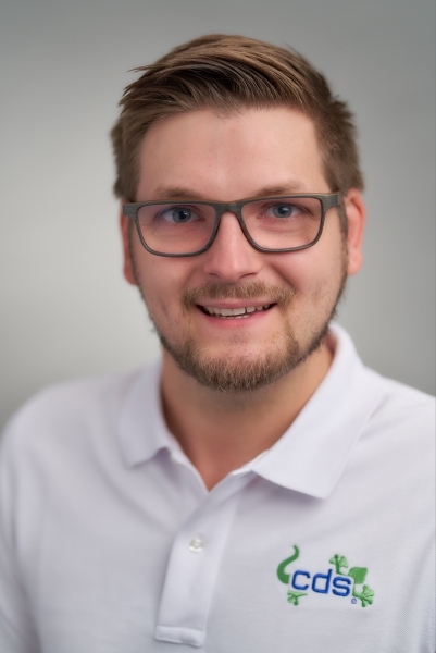 Junger Mann mit Brille, cds-Polohemd und freundlichem Blick.