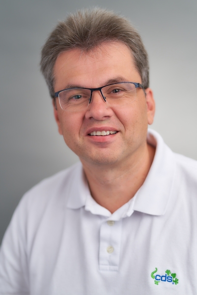 Mann mit Brille, cds-Polohemd und offenem Lächeln.