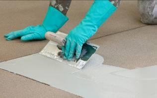 Beschichtung wird mit Handschuhen manuell auf Bodenfläche aufgetragen.