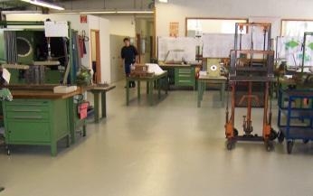 Innenraum mit Werkbänken, Maschinen und hellem Boden.