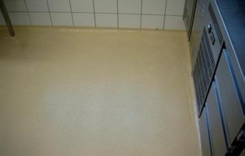 Beiger Boden mit Fliesenwand und Edelstahlmöbeln.