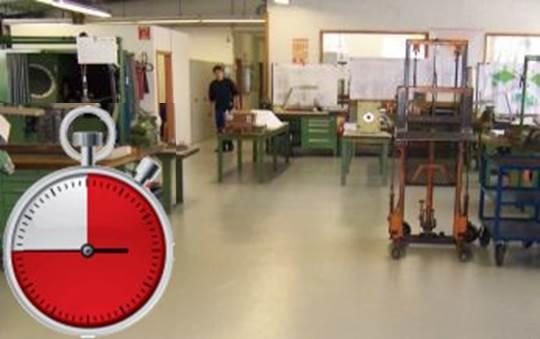 Werkstatt mit Maschinen und eingeblendeter Stoppuhr unten links.