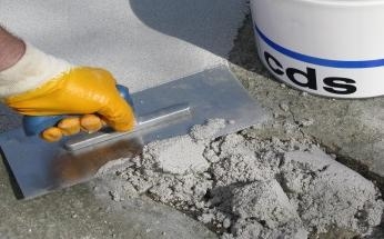 Mörtelmasse wird auf Beton mit Kelle neben cds-Eimer geglättet.