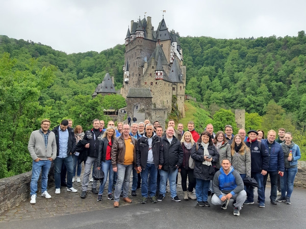 Gruppenfoto vor einer Burg mit vielen Personen im Grünen.